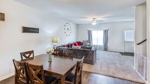 Een moderne woonkamer met een eethoek, een zithoek, een klok en een plafondventilator.