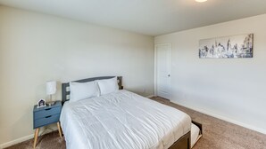 Een slaapkamer met een bed, nachtkastje, lamp en een stadsgezichtschilderij aan de muur.