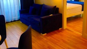 A compact living space with a sofa, a small table, a bed, and an air conditioning unit.