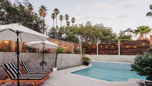 A poolside area with lounge chairs and umbrellas, surrounded by a wooden fence and palm trees. - Family Retreat with Pool and Hot Tub (Vista)