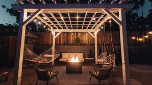 A covered outdoor seating area with a fire pit, two wicker chairs, and a hanging swing. - Family Retreat with Pool and Hot Tub (Vista)