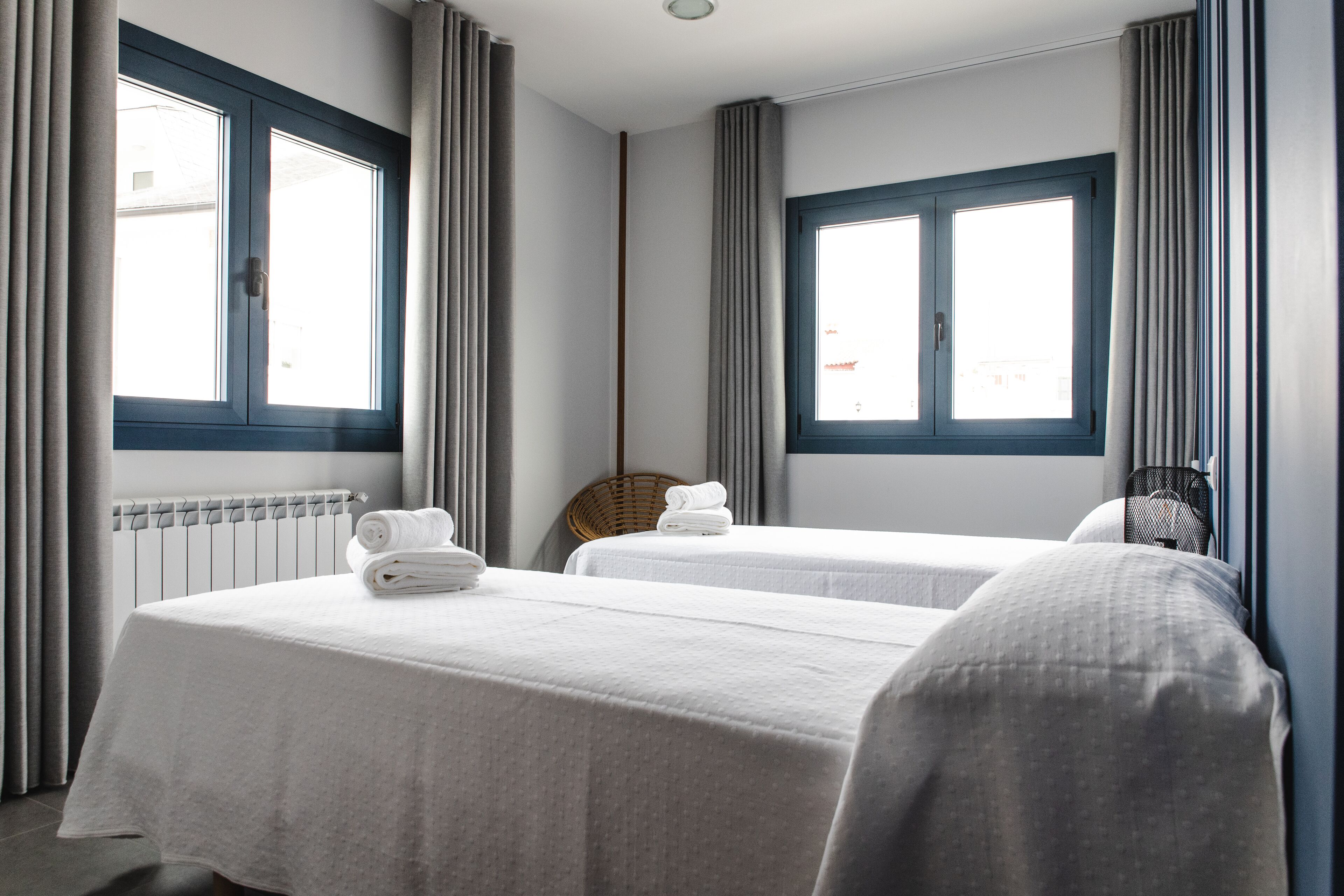 Ein Hotelzimmer mit zwei Betten, einem Heizkörper und großen Fenstern mit Vorhängen.