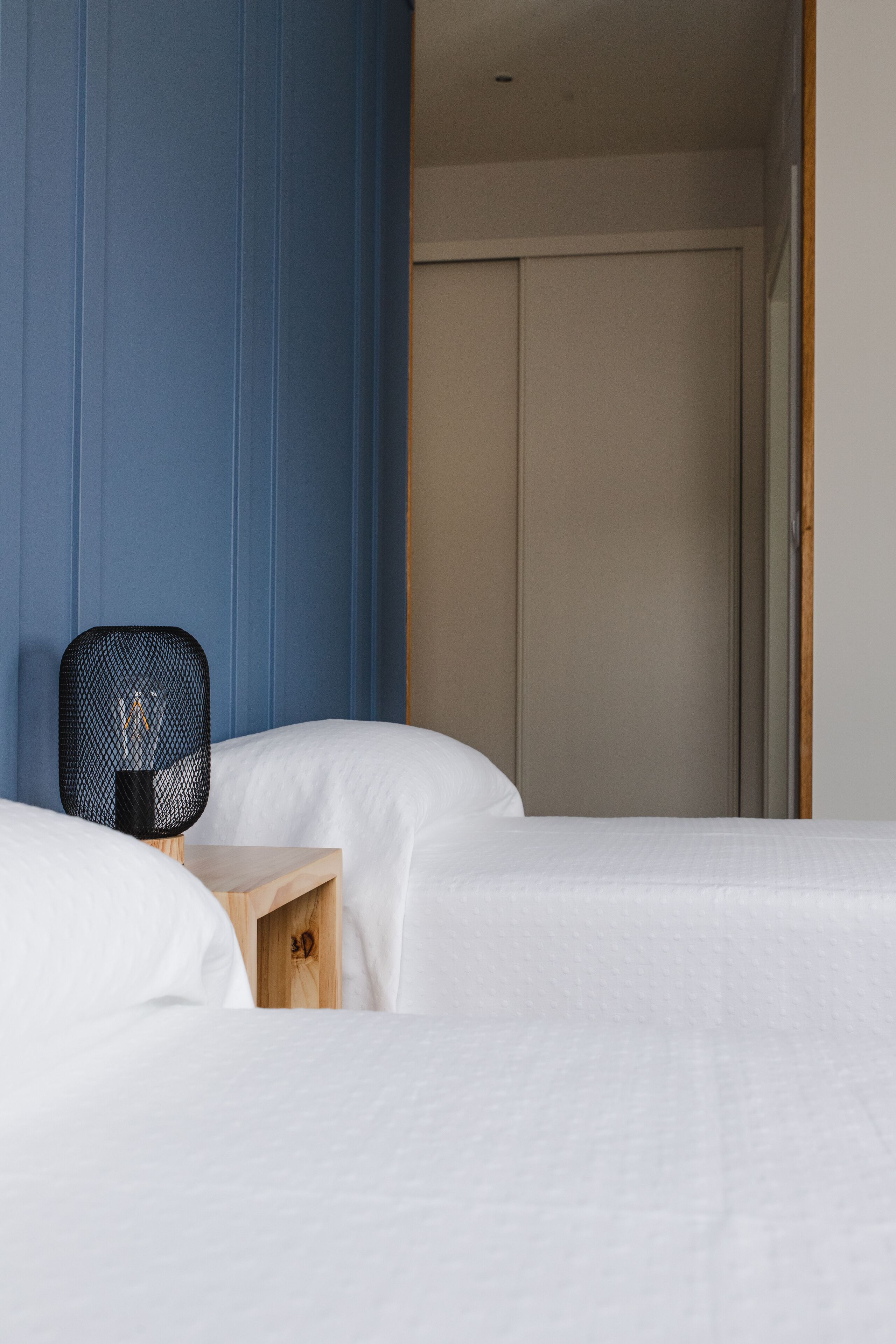 Une chambre d’hôtel avec deux lits, une table de chevet en bois et une chaise noire.
