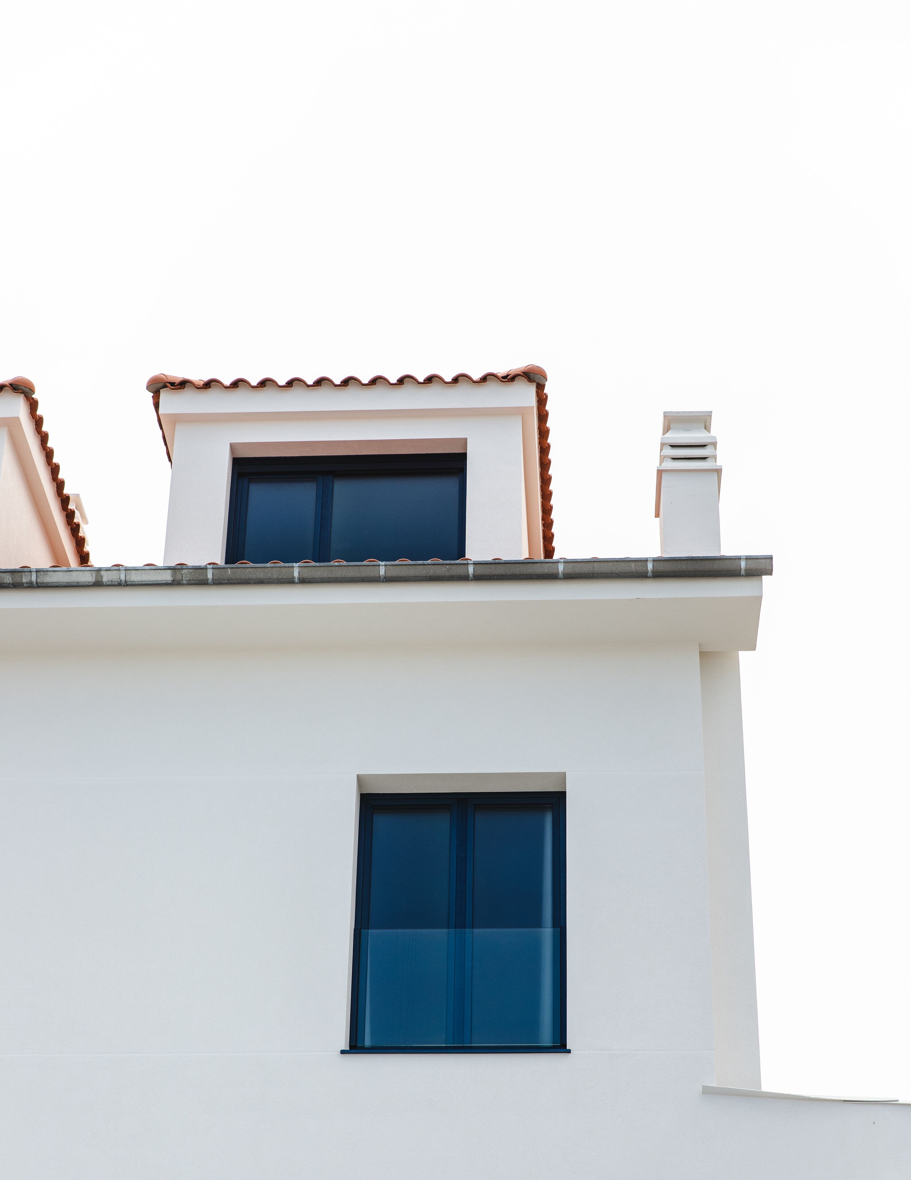 A building with a white facade, a blue window, and a red-tiled roof.