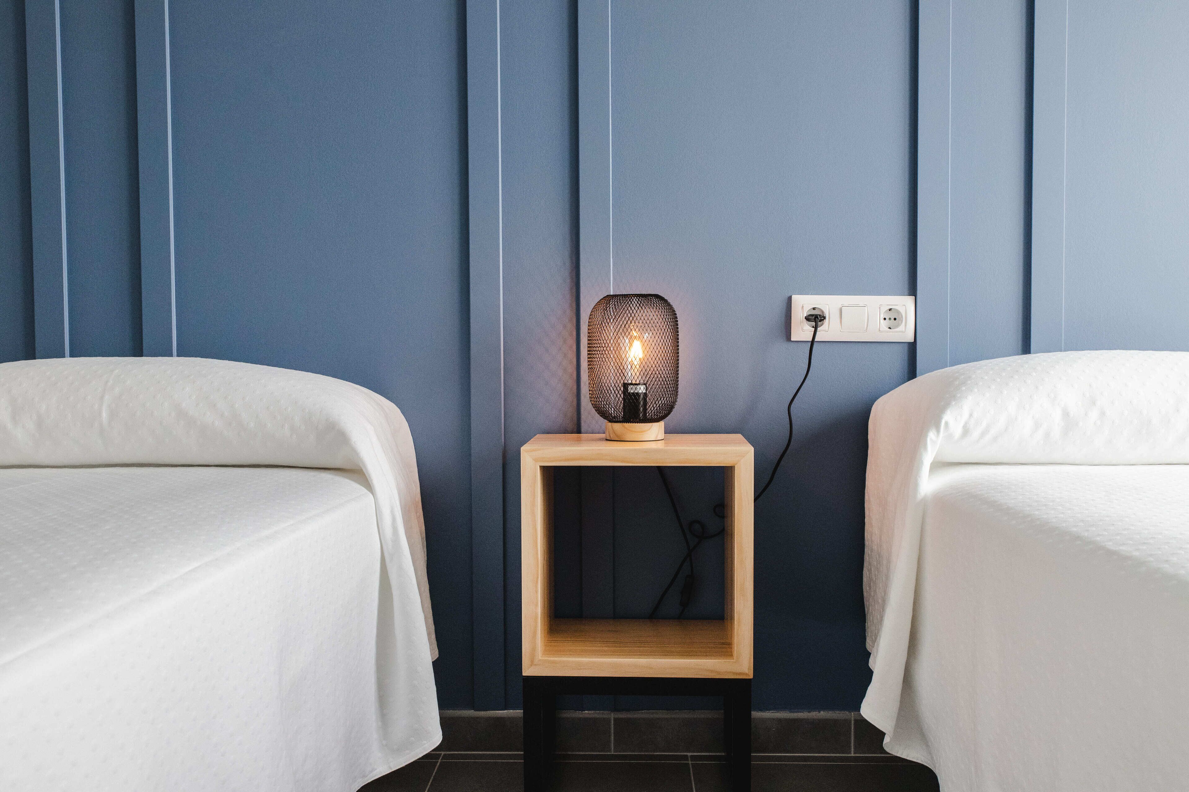 Ett hotellrum med två sängar, ett nattduksbord med en lampa och ett vägguttag.