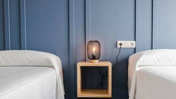 Habitación de hotel con dos camas, una mesita de noche con lámpara y un enchufe en la pared.