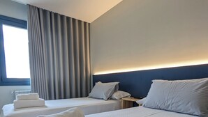 Habitación de hotel con dos camas, una mesita de noche y una ventana con cortinas.