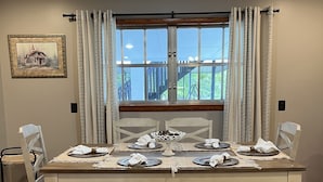 A dining room with a wooden table set for four, white upholstered chairs, a bench, and a window with curtains. - Beautiful quiet retreat near Oneida, Big South Fork, and ATV trails! (Oneida)