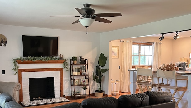 A living room with a fireplace, a black leather sofa, a TV mounted on the wall, and a ceiling fan. - Beautiful quiet retreat near Oneida, Big South Fork, and ATV trails! (Oneida)