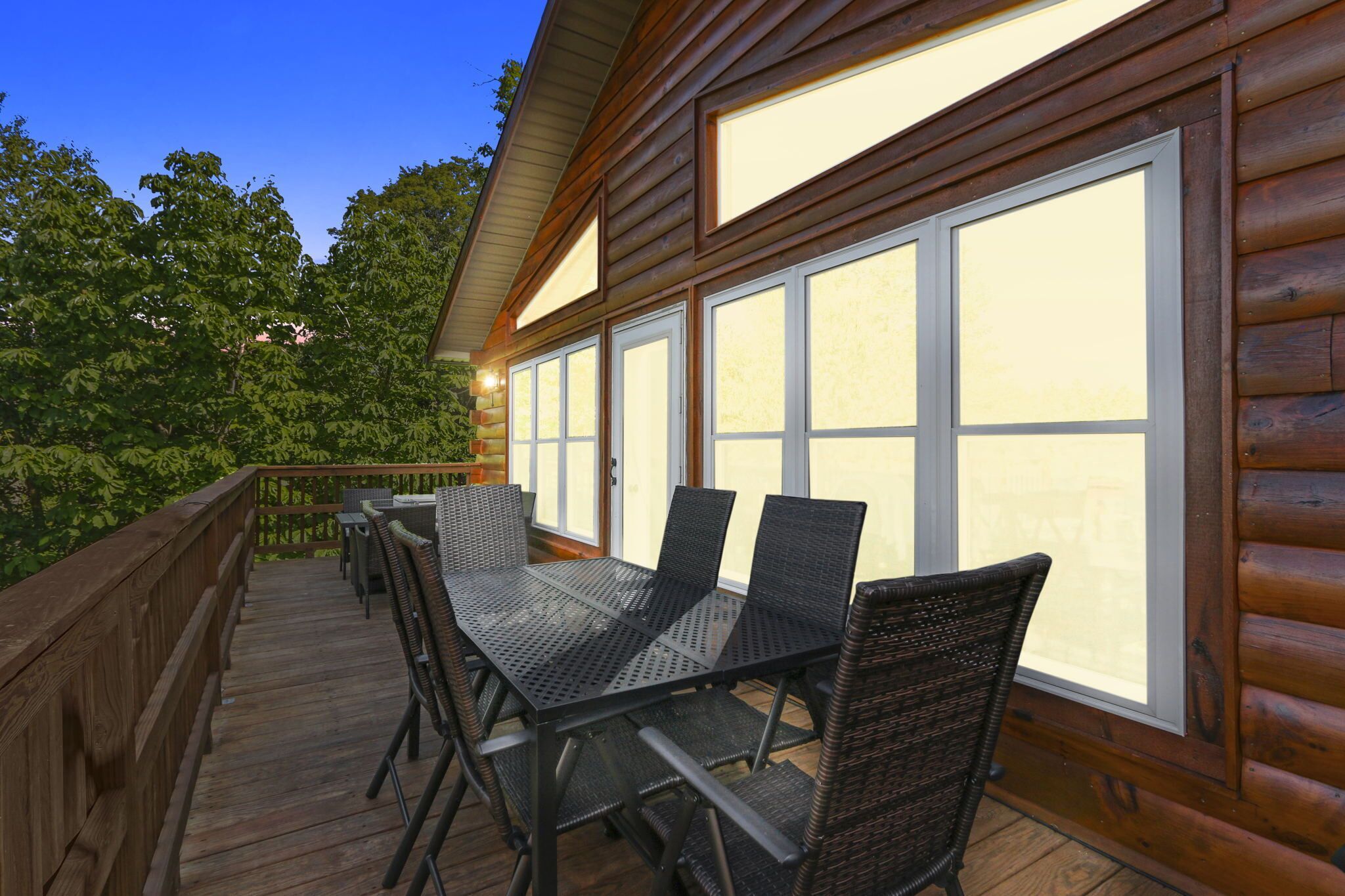 Une terrasse en bois avec une table et des chaises, de grandes fenêtres et une rambarde.