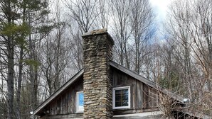Eine rustikale Holzhütte mit einem Steinkamin, Holzfenstern und einer Holzterrasse.