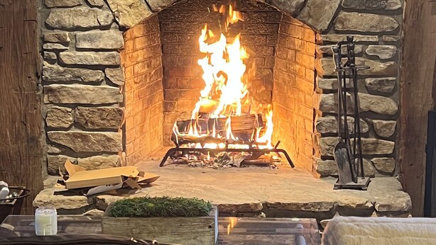 Ein Steinkamin mit Feuer, darüber ein Holzregal und eine Steinwand darum herum.