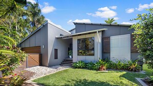 A modern house with a grey exterior, a wooden deck, and a well-maintained lawn. - Mudjimba Escape - Pet friendly, luxury villa w/pool (Sunshine Coast)