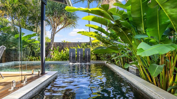 A swimming pool with a waterfall feature surrounded by lush tropical plants. - Mudjimba Escape - Pet friendly, luxury villa w/pool (Sunshine Coast)