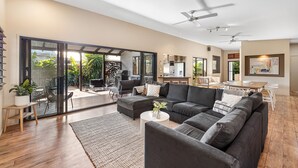 A spacious living area with a large sofa, a dining table, and a kitchen in the background. - Mudjimba Escape - Pet friendly, luxury villa w/pool (Sunshine Coast)