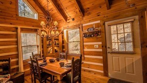 Ein Interieur einer Holzhütte mit Esstisch, Stühlen, einer Chandelierleuchtre und einer Tür mit Fenster.