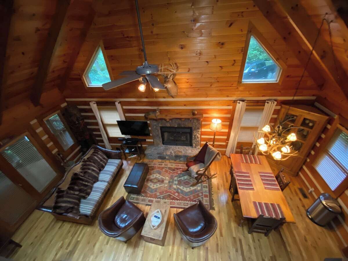 L’intérieur chaleureux d’un chalet avec une cheminée, un plancher en bois, un canapé, des fauteuils, une table à manger et deux puits de lumière.