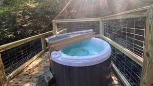 Ein Whirlpool in einer bewaldeten Gegend mit einer Holzterrasse und Metallgeländer.