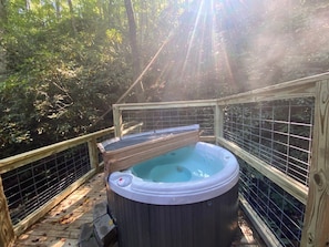 A hot tub in a wooded area with a wooden deck and metal railing.