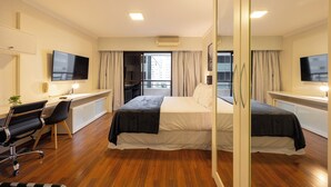 A modern hotel room with a large bed, a desk with a computer, a chair, and a TV. - GPP - Grand Plaza Paulista By Anora Spaces (São Paulo)