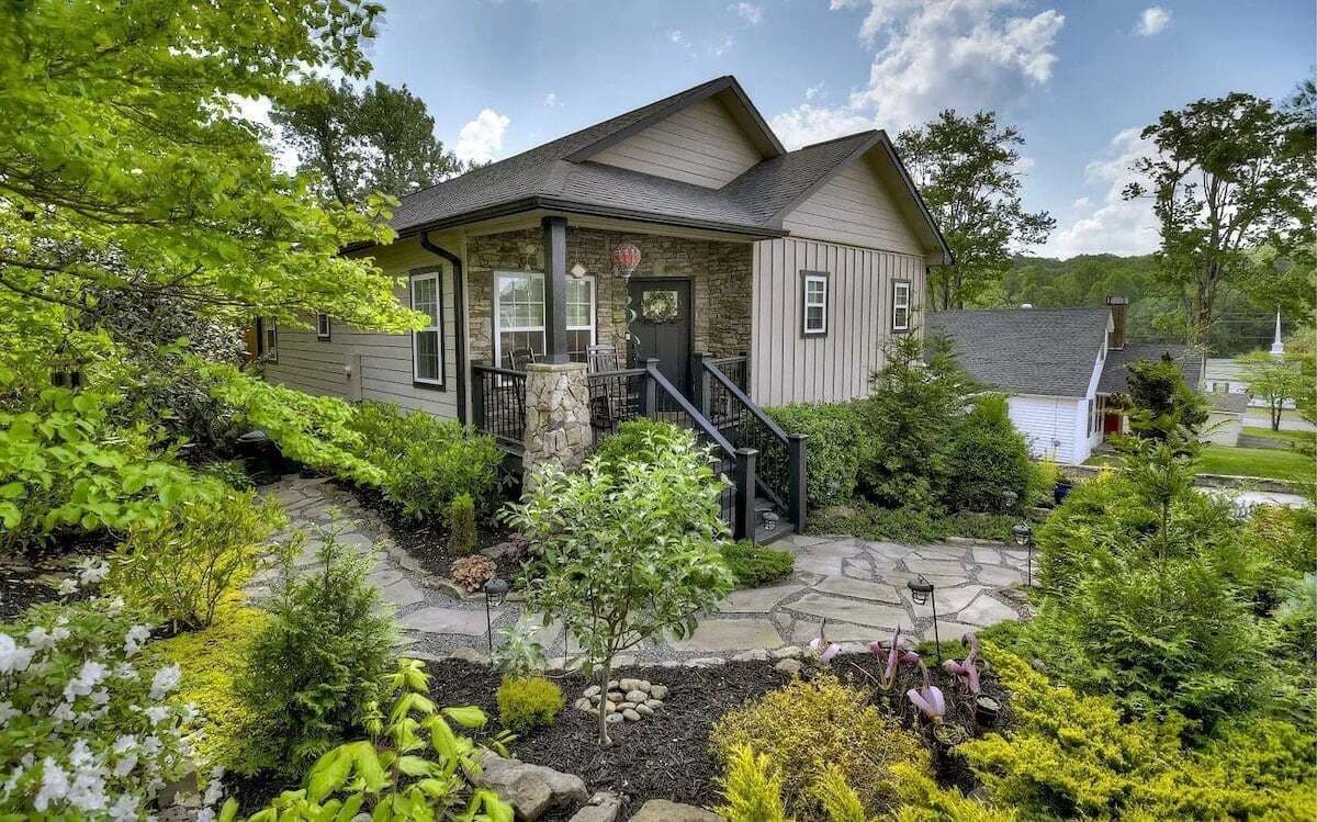 A single-story house with a stone pathway leading to the front door, surrounded by lush greenery and a small garden.