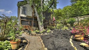 Ein zweistöckiges Haus mit einer Holzterrasse und einem Garten mit verschiedenen Pflanzen und einem Kiesweg.