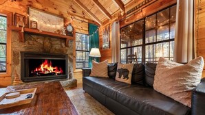 A cozy cabin interior with a stone fireplace, leather sofa with bear-themed pillows, and a wooden coffee table. - Boho Bear Cave of Blue Ridge (Blue Ridge)