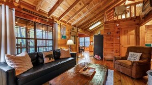 A cozy cabin interior with a wooden ceiling, a black leather sofa, a wooden coffee table, and a brown armchair. - Boho Bear Cave of Blue Ridge (Blue Ridge)