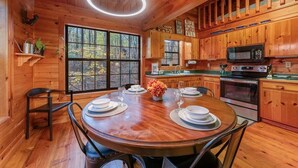 A wooden cabin interior with a dining table set for four, a kitchen with wooden cabinets, a microwave, and an oven. - Boho Bear Cave of Blue Ridge (Blue Ridge)