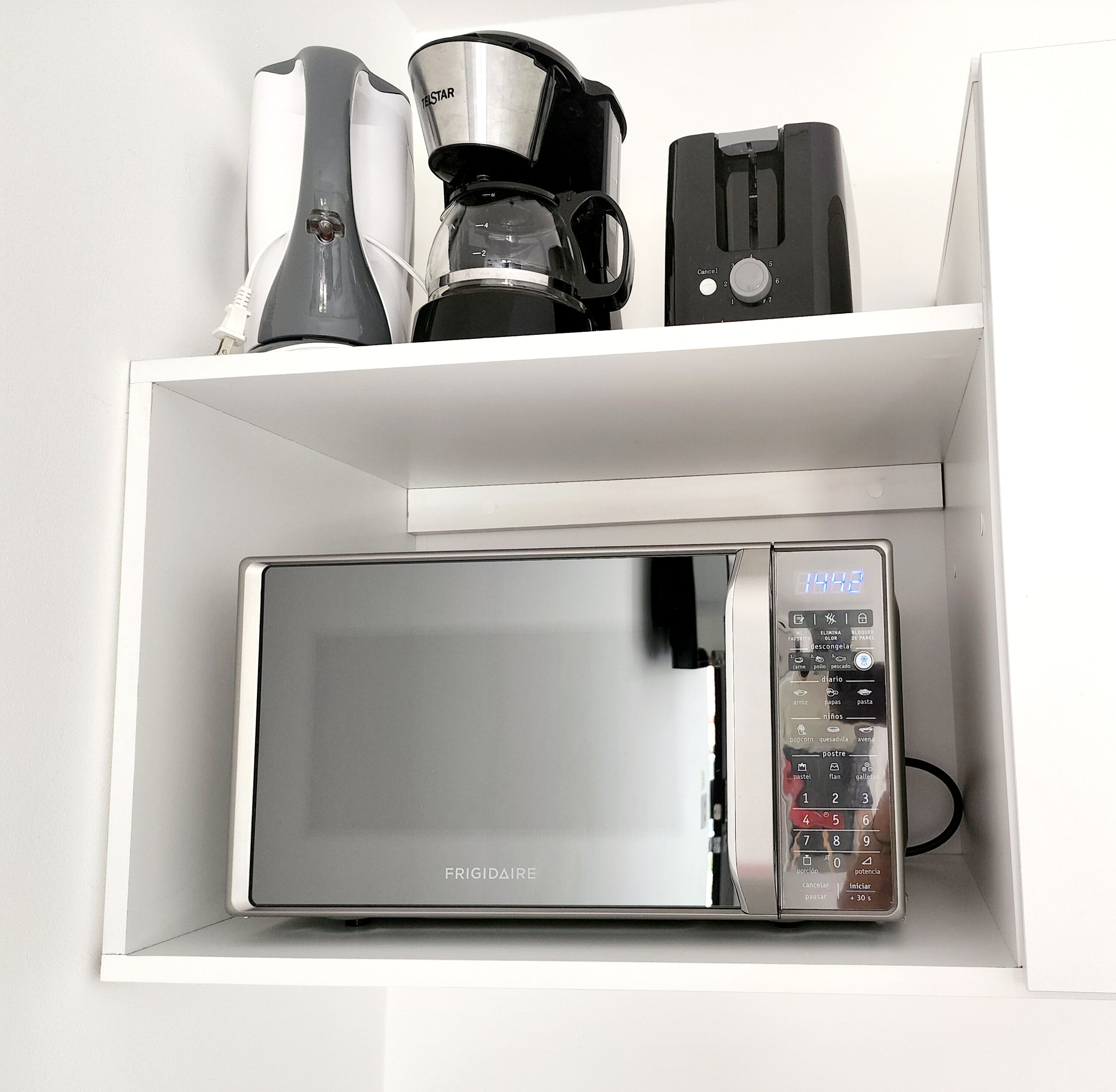A kitchen with a microwave, coffee maker, and toaster on a white shelf.
