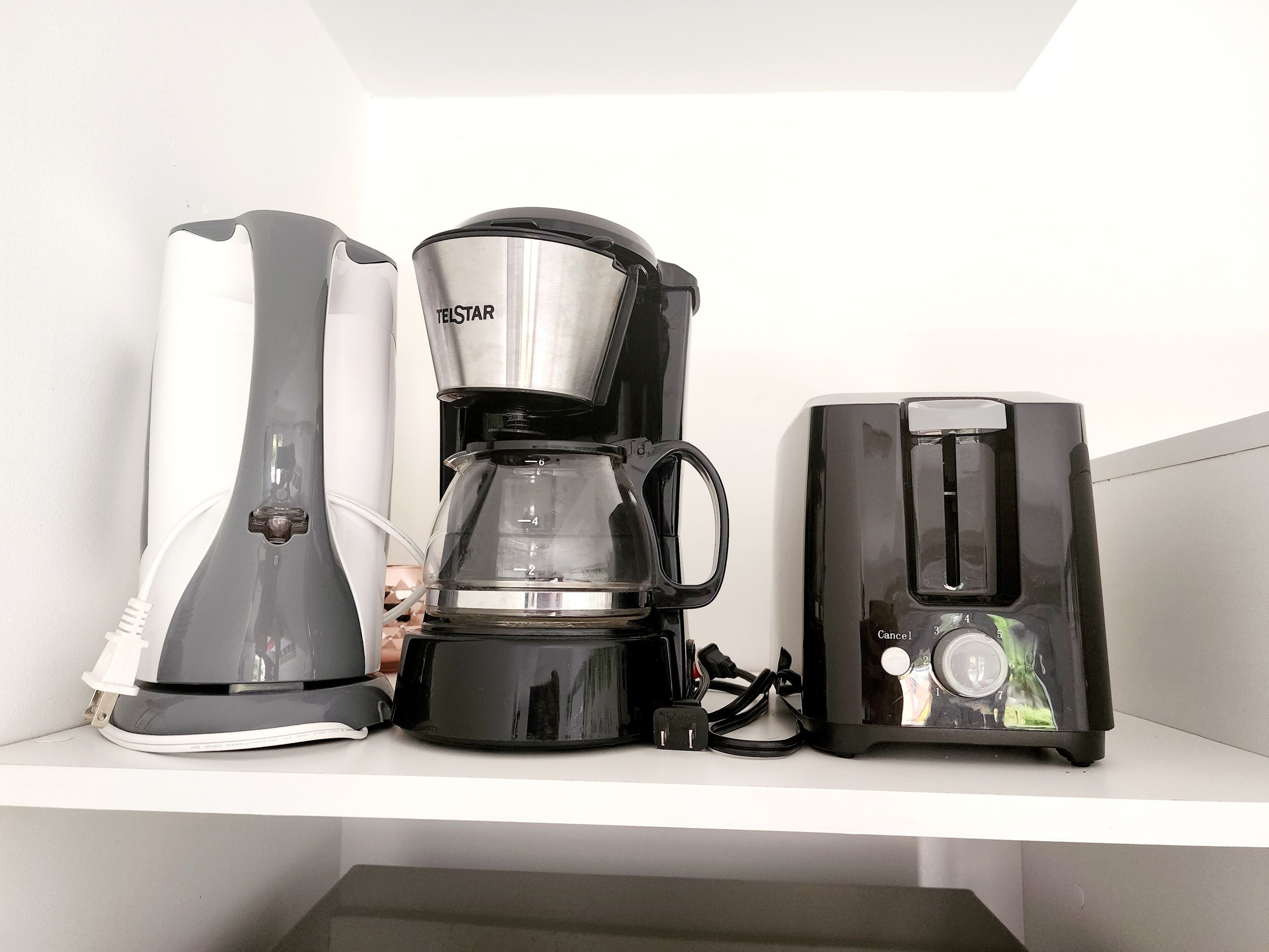 A coffee maker, a toaster, and a kettle on a white shelf.