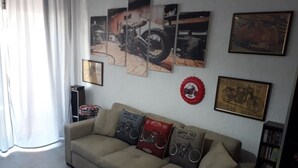 A living room with a beige sofa, three vintage race-themed cushions, a motorcycle painting, and a red circular decoration on the wall. - Beach and relax. history and events. Everything at your fingertips. (Francavilla al Mare)