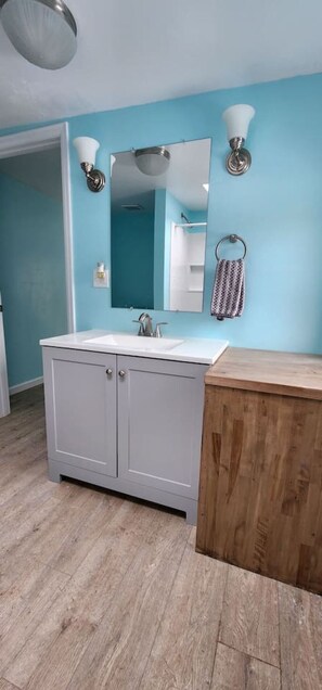 Une salle de bain avec un lavabo blanc, des meubles gris, un meuble-lavabo en bois, un miroir et un porte-serviettes.