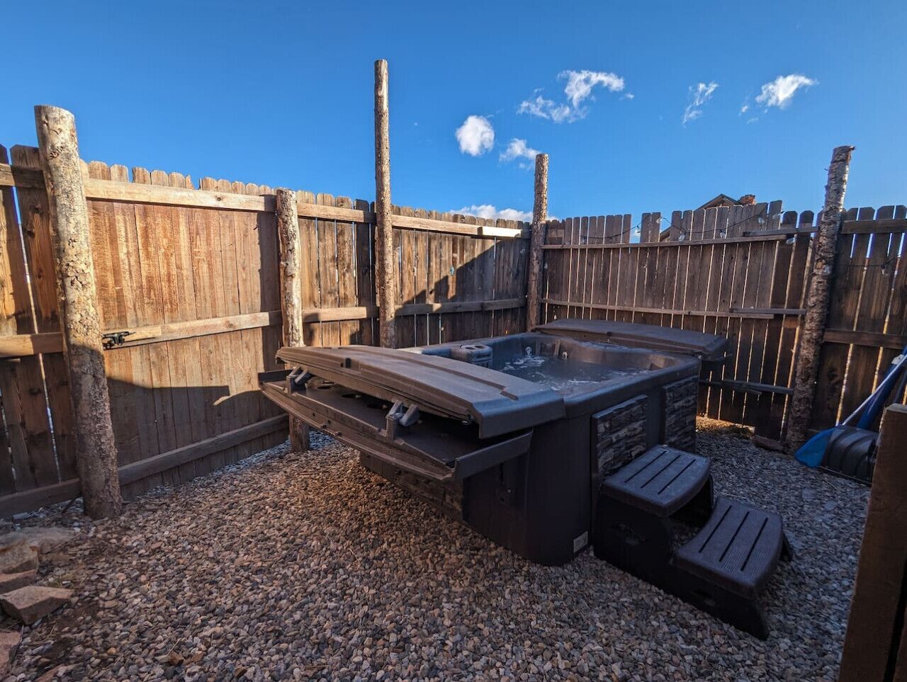 Ein Whirlpool mit Holzterrasse und Steinbänken, umgeben von einem Holzzaun und Kiesboden.