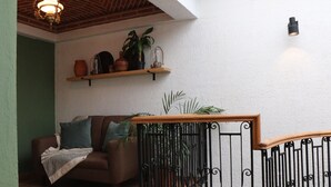 A cozy living area with a brown sofa, a wooden coffee table, and a potted plant. There is a staircase with a black railing and a light fixture on the wall. - Casa Madera (Lagos de Moreno)