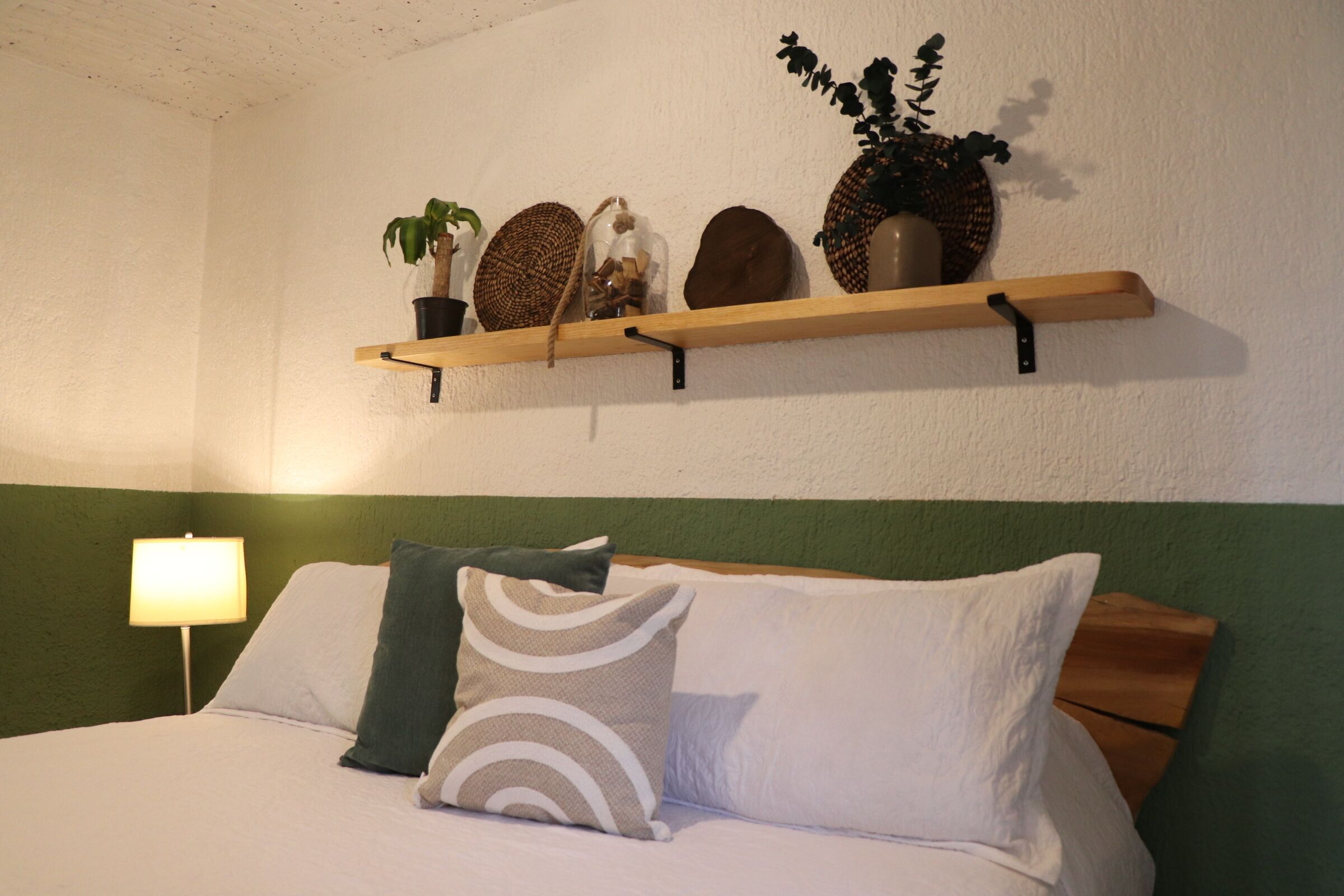 Ein ordentlich bezogenes Bett mit Kissen, einer Nachttischlampe und einem Regal mit Dekoration.