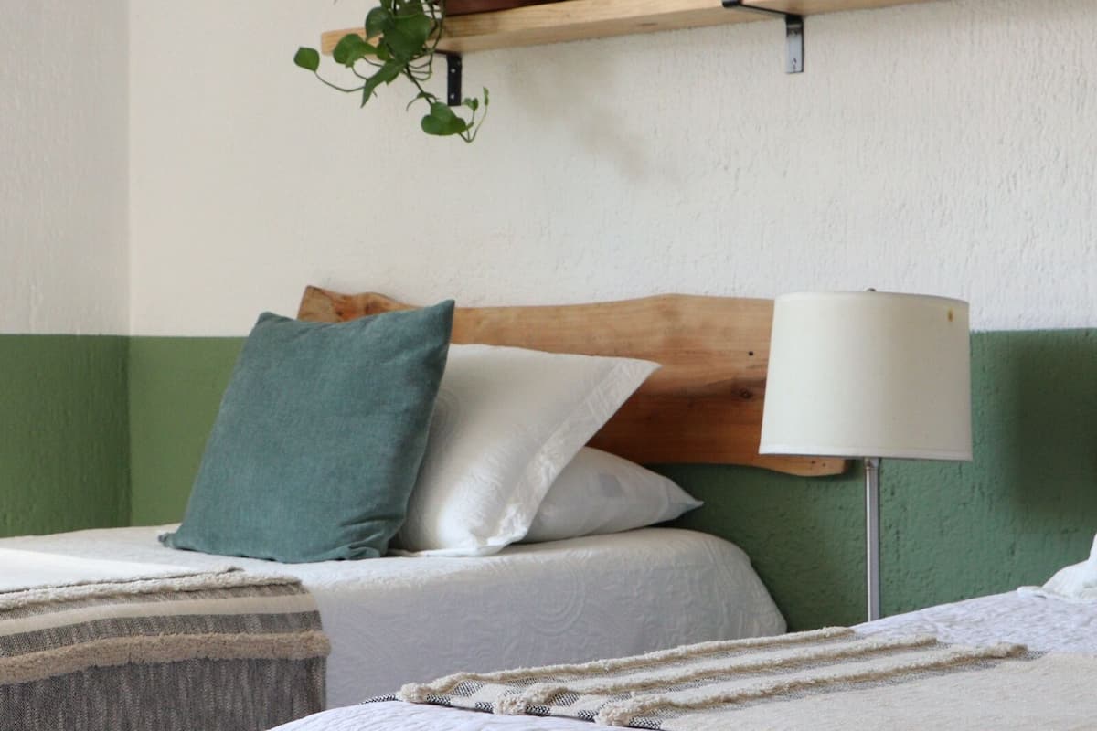 A hotel room with a bed, a bedside table, a lamp, and a shelf with decorative items.