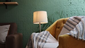 A room with a green textured wall, a brown armchair, a yellow armchair with a striped blanket, and a floor lamp. - Casa Madera (Lagos de Moreno)