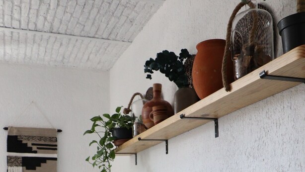 A room with two beds, a wooden headboard, a shelf with plants and pottery, and a wall with a patterned tapestry. - Casa Madera (Lagos de Moreno)