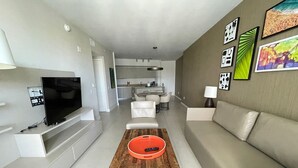 Ett modernt vardagsrum med en platt-TV, ett soffbord i trä och en beige soffa.