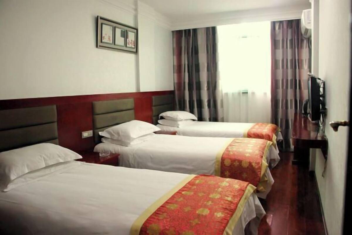 Een hotelkamer met drie bedden, een televisie en een raam met gordijnen.
