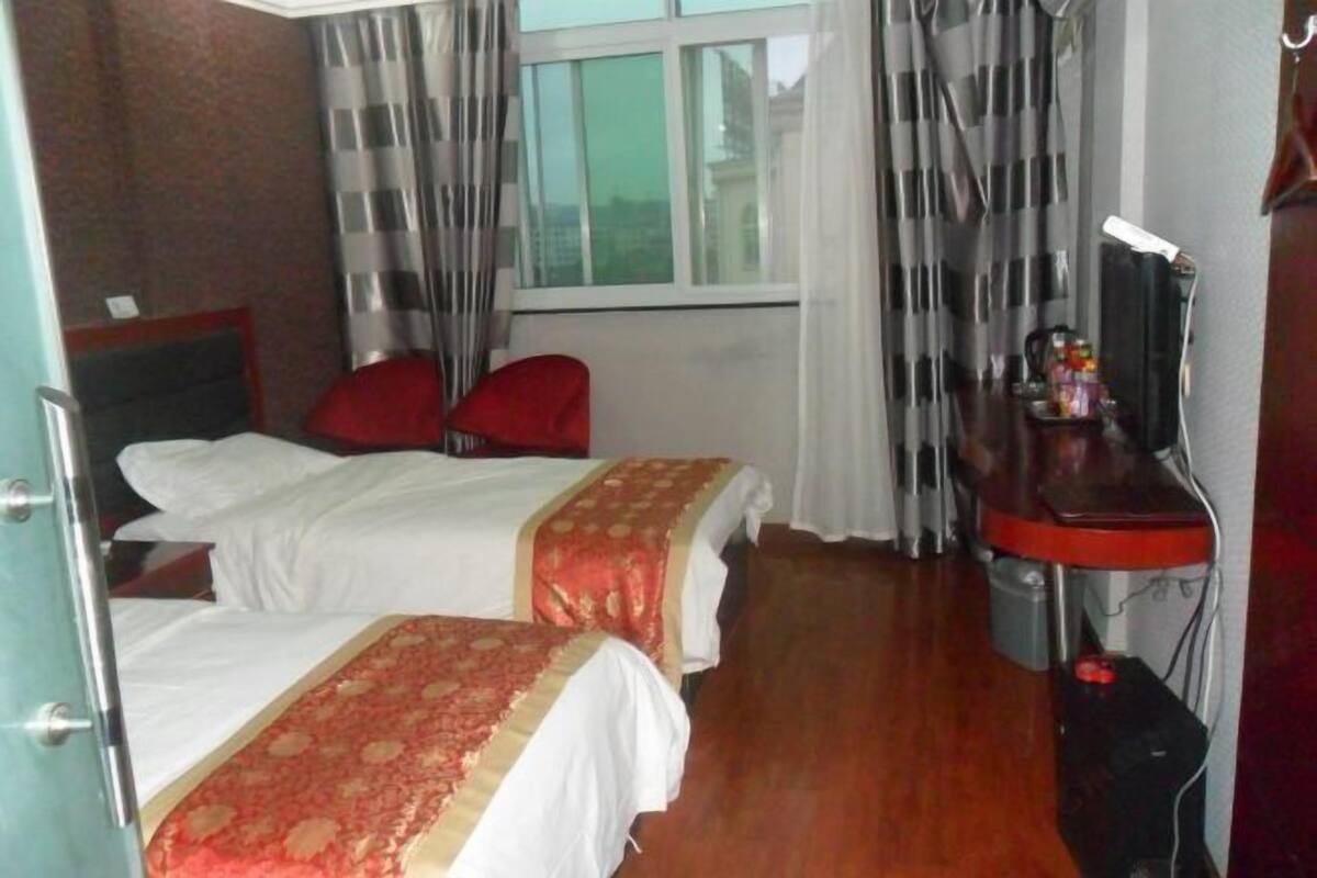 Een hotelkamer met twee bedden, een bureau met een computer, een stoel en een raam met gordijnen.