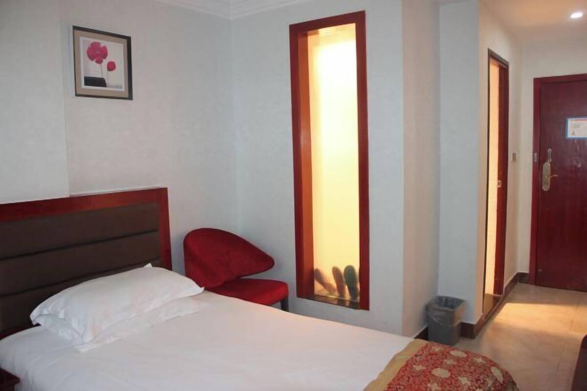 Een hotelkamer met een bed, een rode stoel, een deur met spiegel en een lijst aan de muur.