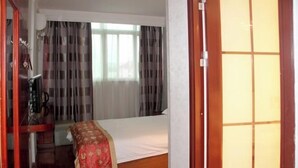 Une chambre d’hôtel avec un lit, une armoire en bois et une fenêtre avec des rideaux.