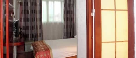 Habitación de hotel con una cama, un armario de madera y una ventana con cortinas.