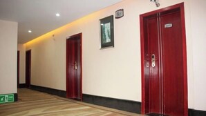 Un couloir avec des portes rouges, un panneau de sortie vert et un tableau encadré accroché au mur.