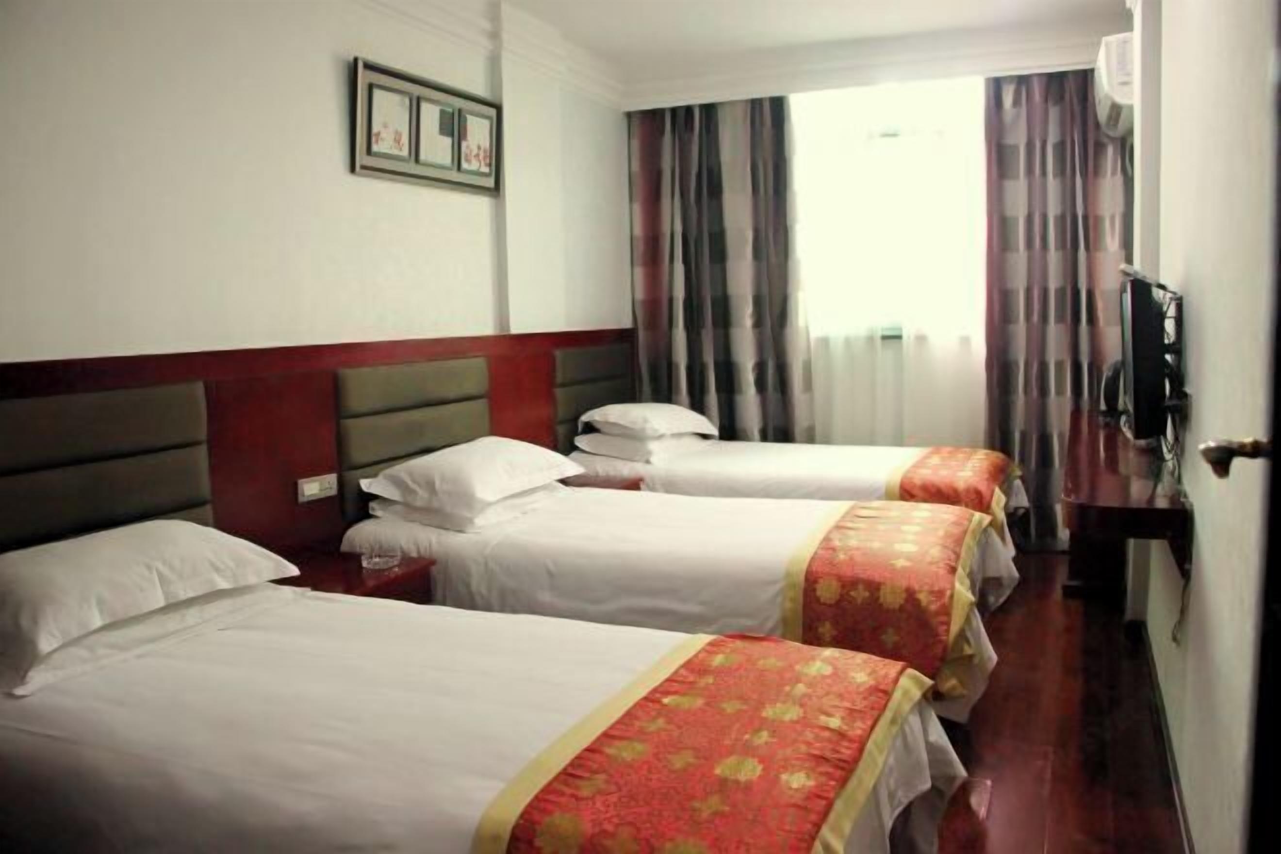 Quarto de hotel com três camas, televisão e janela com cortinas.