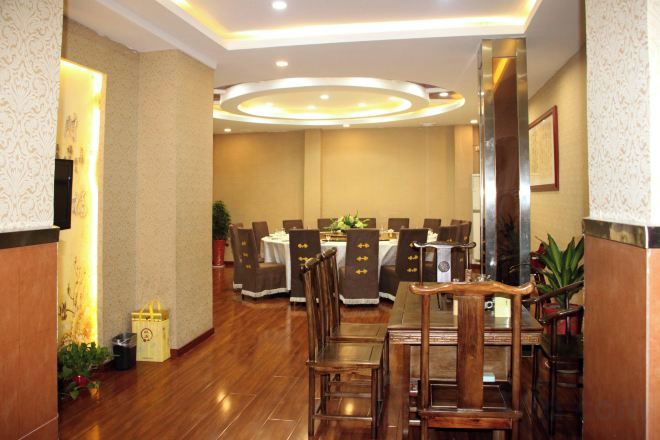 A hotel dining area with multiple tables and chairs, a wooden floor, and a modern ceiling design.