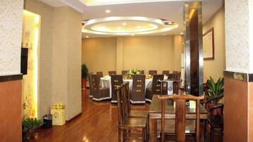 A hotel dining area with multiple tables and chairs, a wooden floor, and a modern ceiling design.