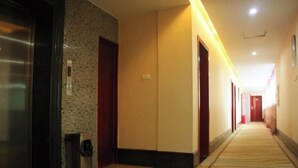Un couloir d’hôtel avec un sol recouvert de moquette, des portes en bois et un mur carrelé d’un côté.
